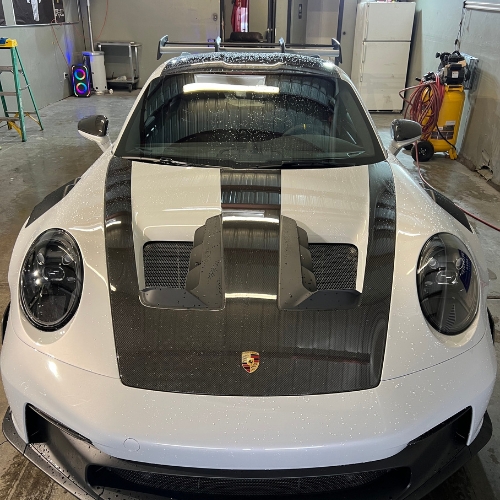 White Porsche sports car with carbon fiber hood in workshop garage setting