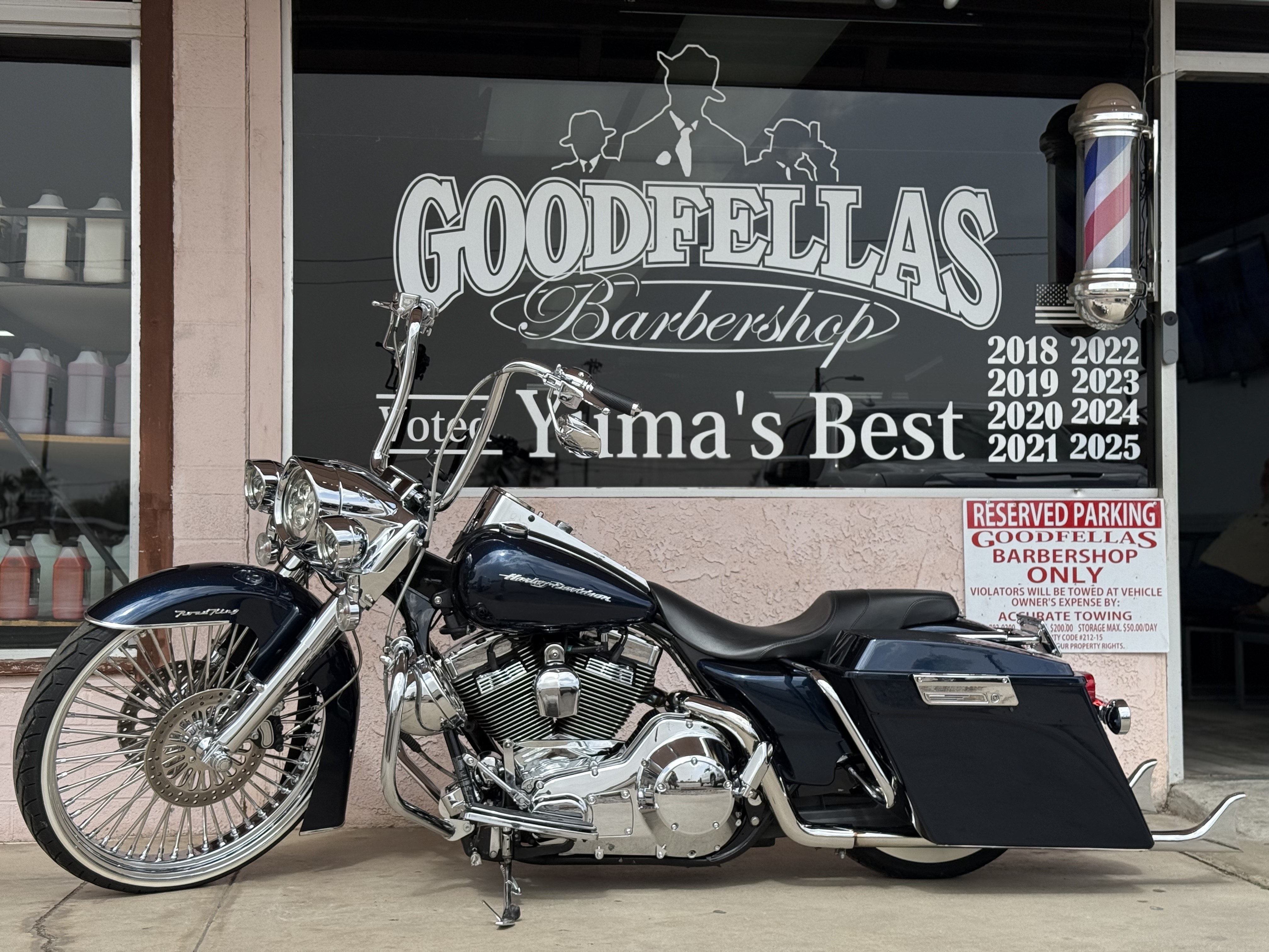 Chrome motorcycle parked outside Goodfellas Barbershop storefront with award years displayed.