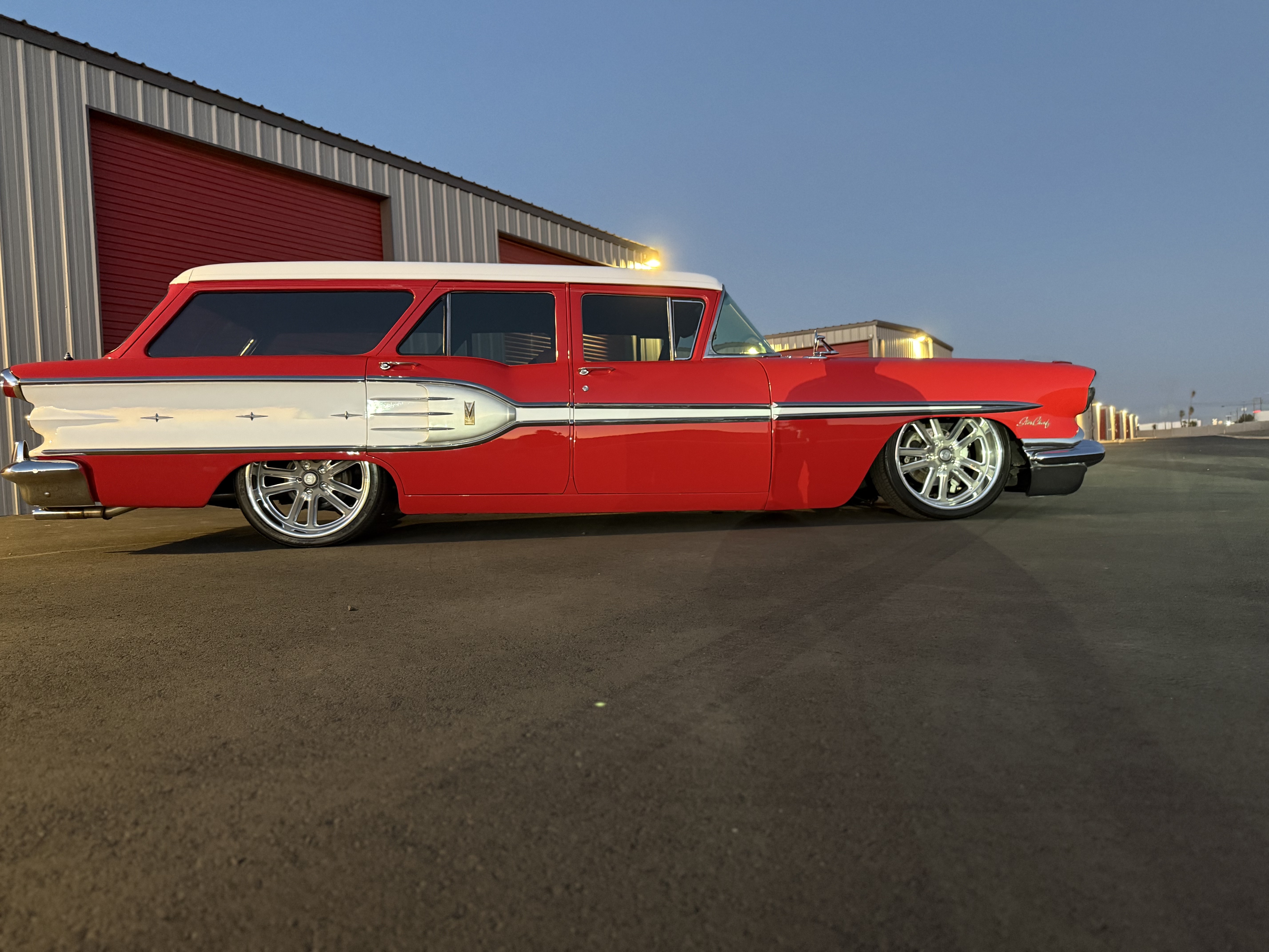 Red and white 1957 Ford classic station wagon with custom wheels parked at warehouse
