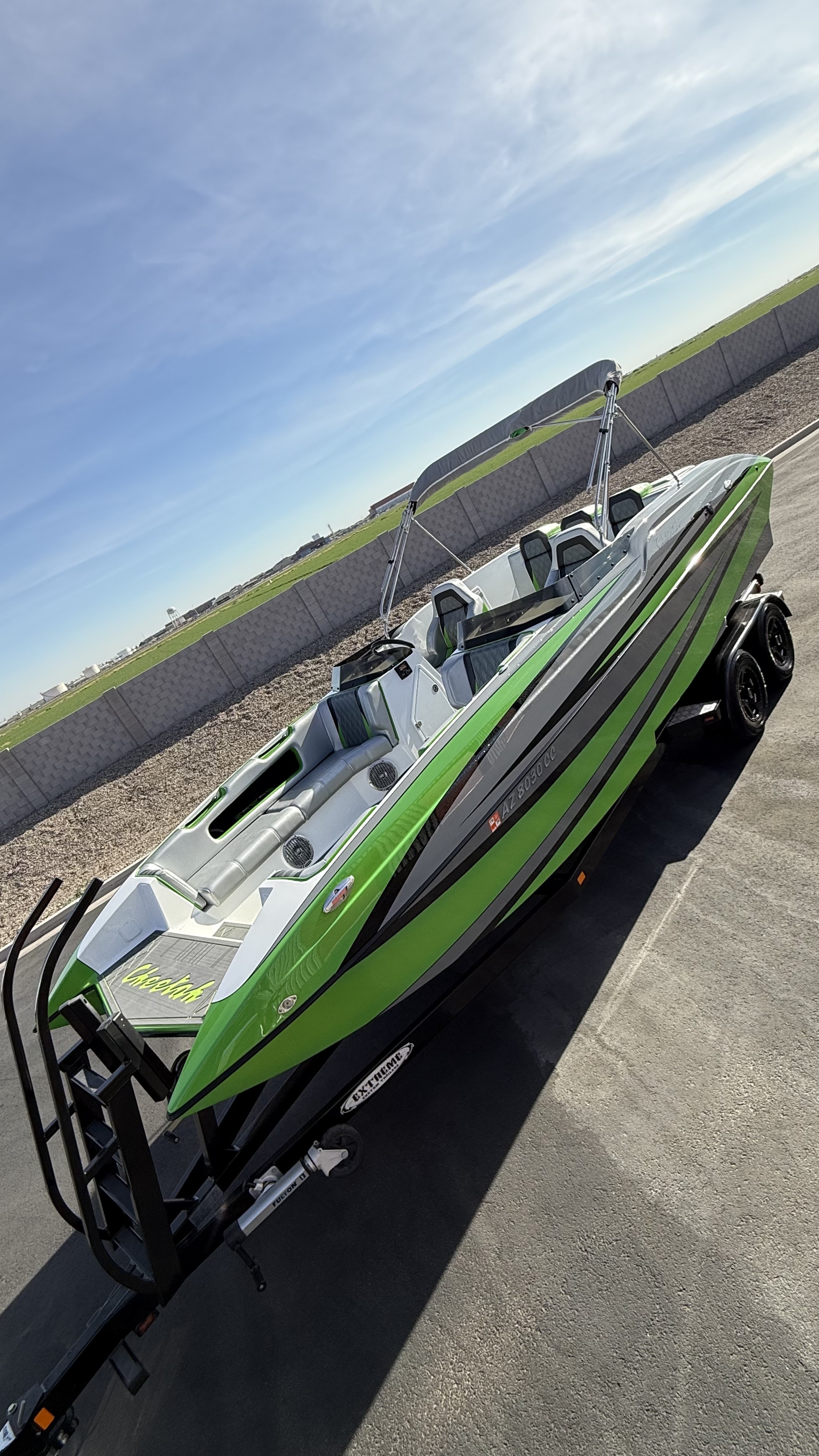 Three speedboats lined up on pavement with green dikes and blue sky behind.