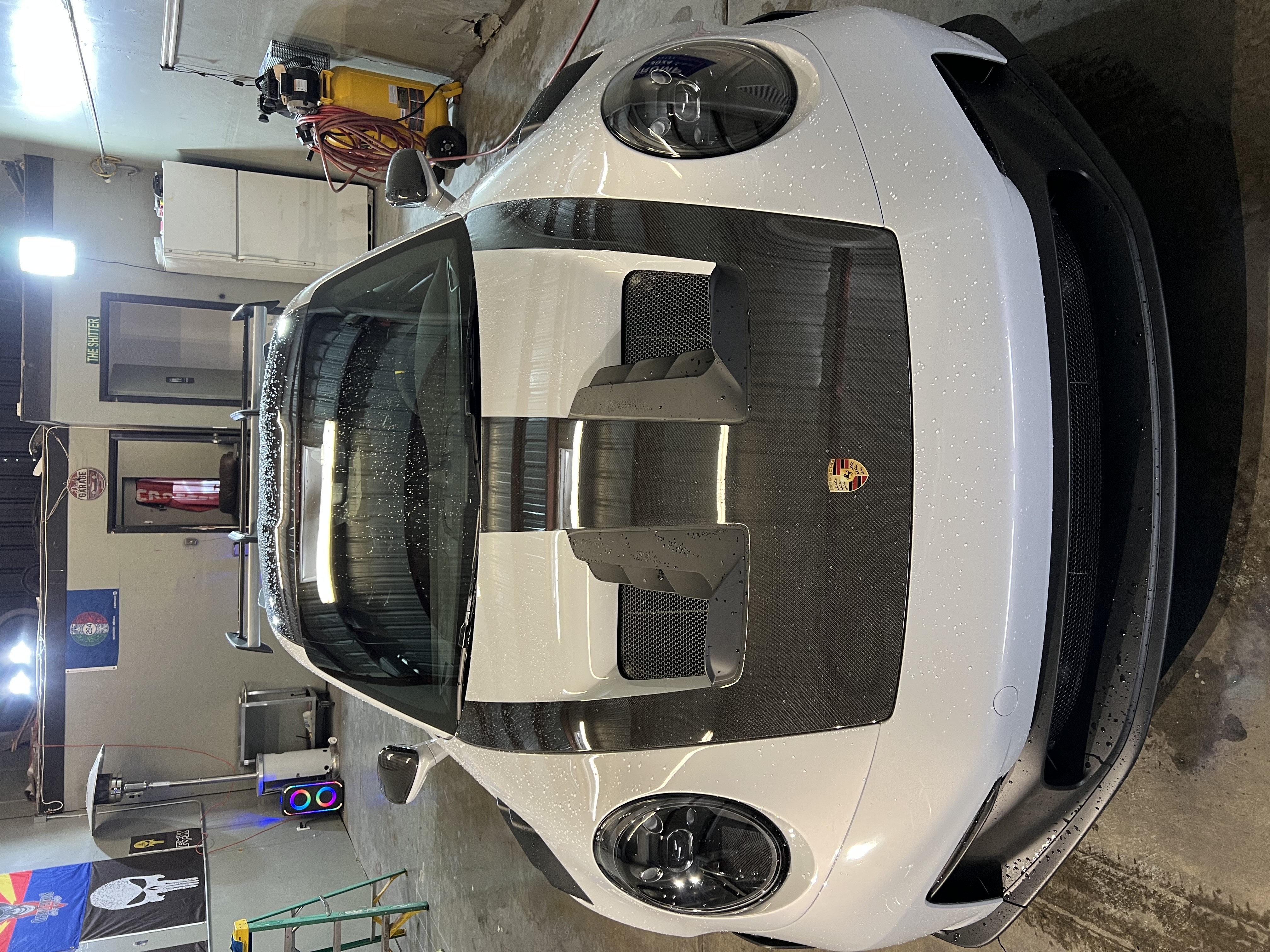 White Porsche sports car with black carbon fiber hood in garage workshop setting