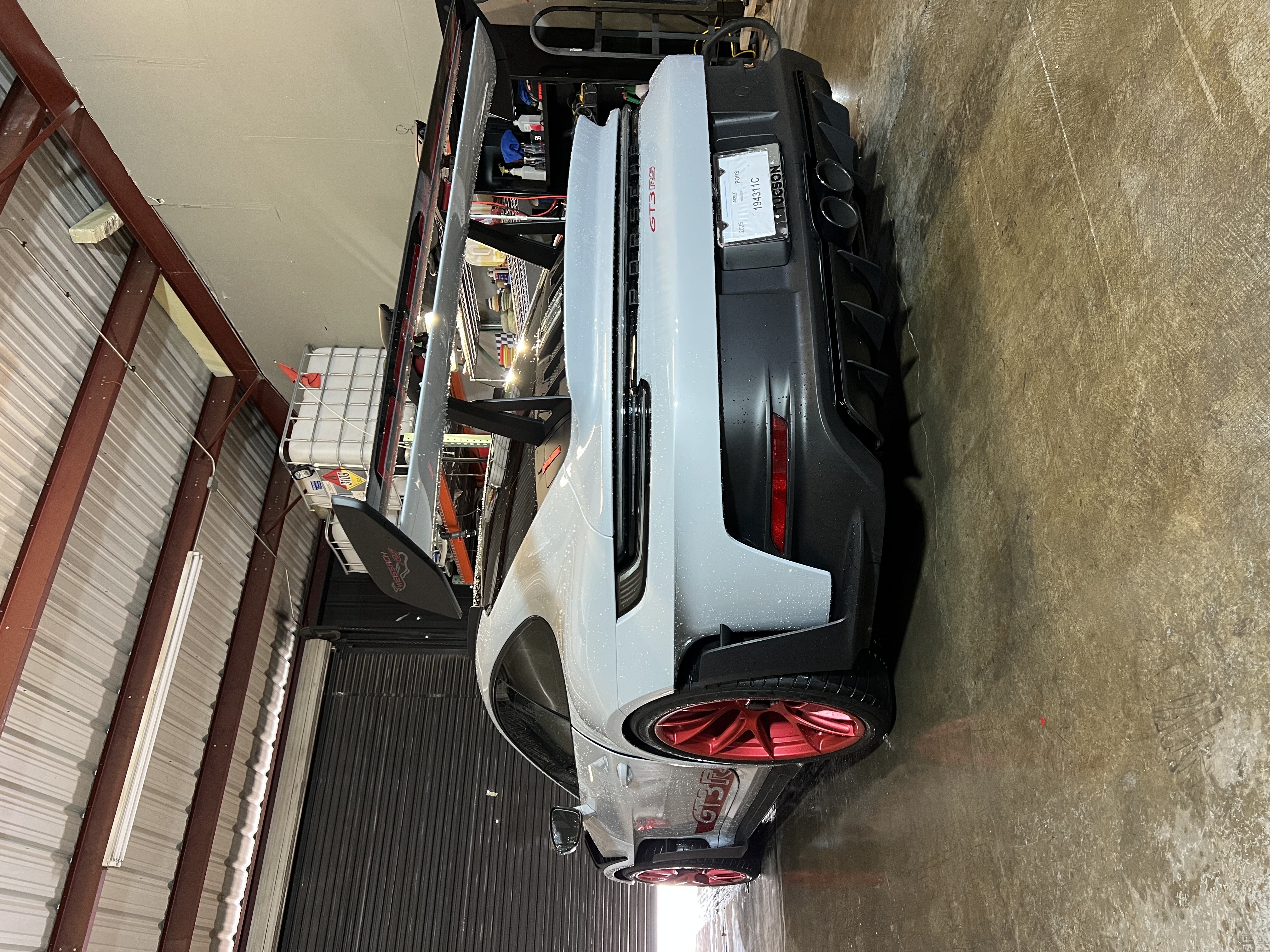 White Porsche GT3 with red wheels in industrial garage workshop setting.