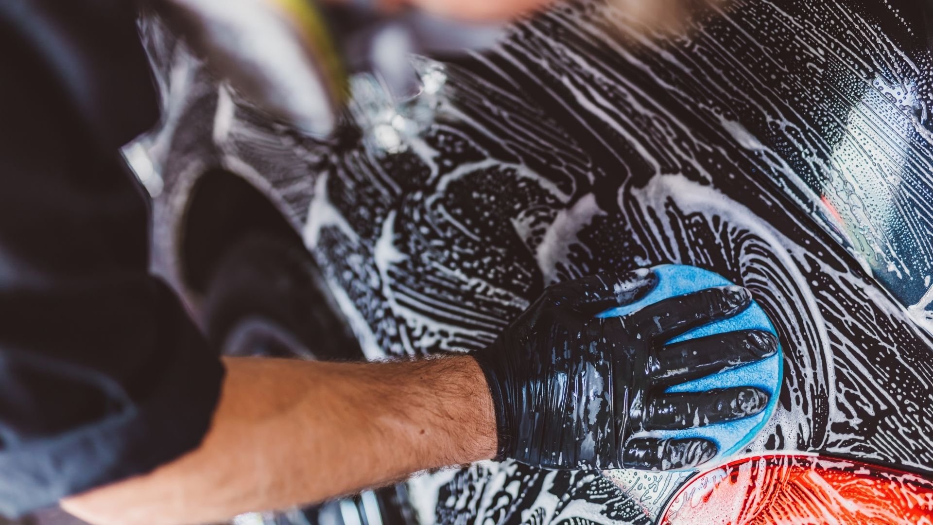 Hand washing a black and white vehicle with blue and red sponge detail