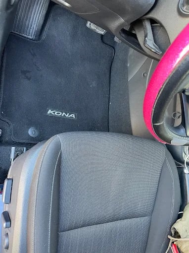 Car interior showing gray seat and black Kona floor mat with pink trim