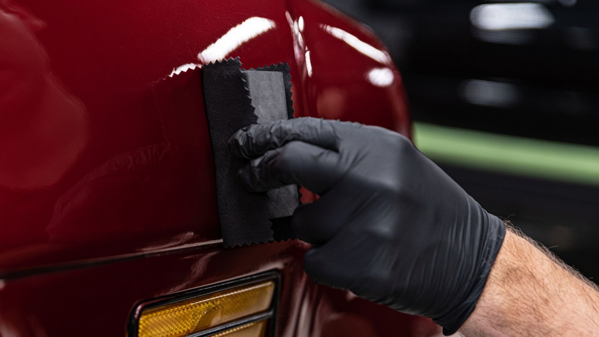 Hand in black glove polishing red car surface with gray cloth pad