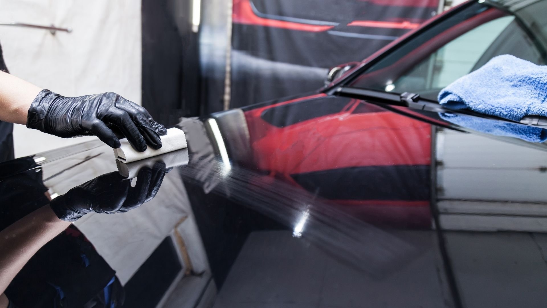 Person in black gloves polishing red car with white cloth during detailing service