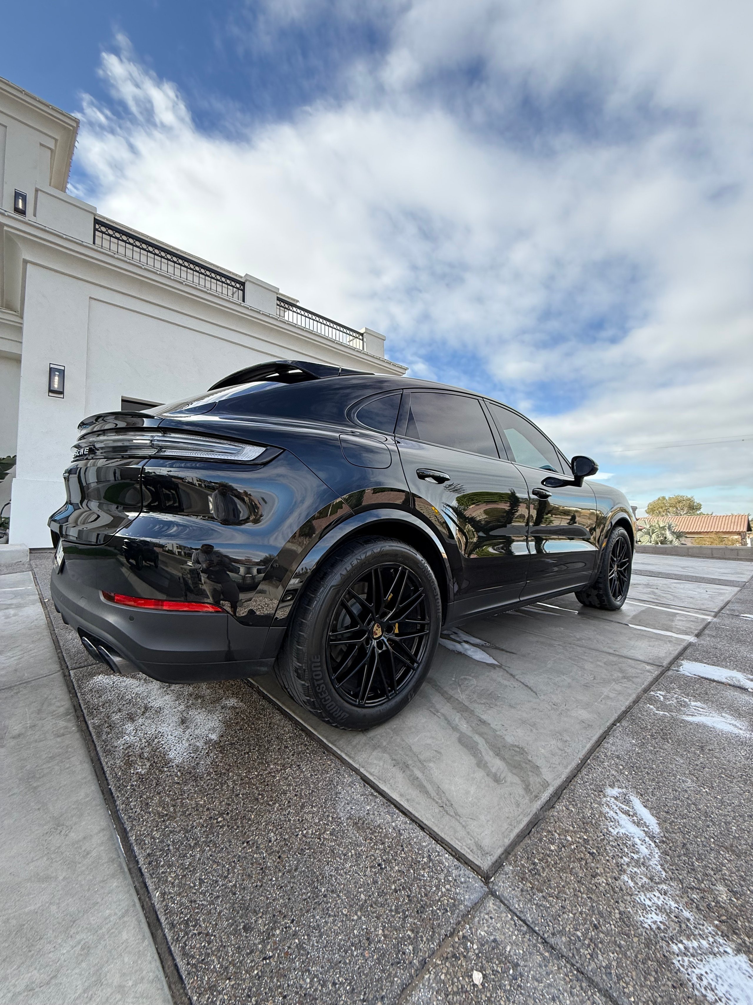 Black electric SUV parked outside modern white house under cloudy blue sky